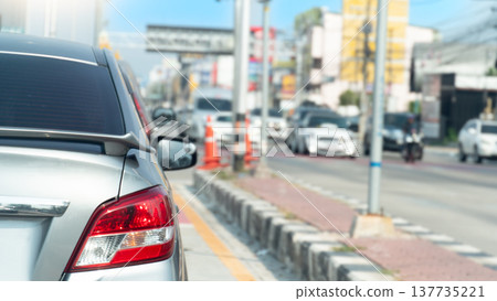 Rear side of car with turn on brake light in the bright sky. Side of the road have median strip paved and lined with lampposts. Many cars are stuck waiting at traffic lights and in the city. Rear side of car with turn on brake light in the bright sky. Side of the road have median strip paved and lined with lampposts. Many cars are stuck waiting at traffic lights and in the city. 137735221