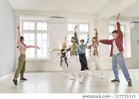 Smiling young people training modern dance moves together in studio with female choreographer. Smiling young people training modern dance moves together in studio with female choreographer. 137735315