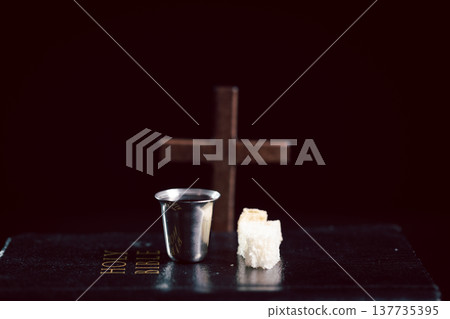 Still life of communion bread and silver cup of red wine with wooden cross on dark table, symbolizing Christian Eucharist, worship, faith, sacrifice and remembrance with copy space. Still life of communion bread and silver cup of red wine with wooden cross on dark table, symbolizing Christian Eucharist, worship, faith, sacrifice and remembrance with copy space. 137735395