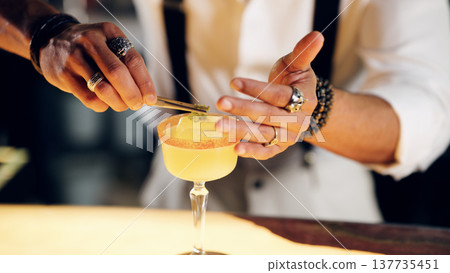 Bartender garnishing cocktail with tweezers at a bar Bartender garnishing cocktail with tweezers at a bar 137735451