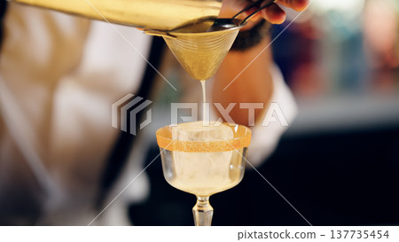 Bartender straining cocktail into glass with ice Bartender straining cocktail into glass with ice 137735454