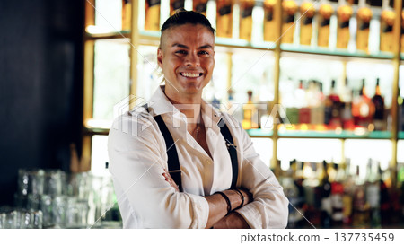 Experienced bartender smiling, standing with arms crossed in bar 137735459