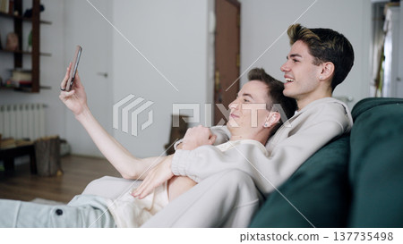 Gay couple relaxing on sofa taking selfie 137735498