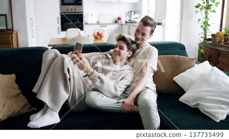 Gay couple relaxing on sofa watching smartphone together 137735499