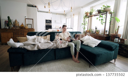 Gay couple relaxing on sofa with devices Gay couple relaxing on sofa with devices 137735502