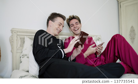 Gay couple laughing together in bed with smartphone 137735541
