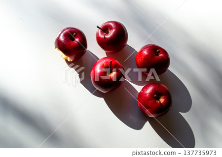 Five red ripe apples lying on a white table and their shadows Five red ripe apples lying on a white table and their shadows 137735973