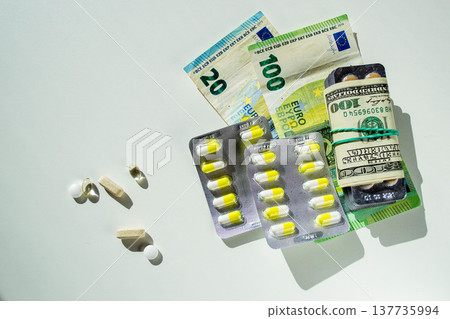 Jelly capsules and hard tablets of vitamin D on dollar bills on a white table Jelly capsules and hard tablets of vitamin D on dollar bills on a white table 137735994