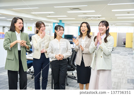 A group of female employees chatting and communicating in a brightly lit office. 137736351