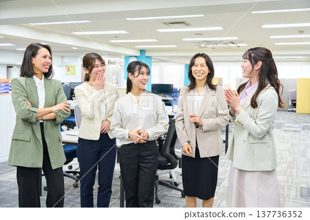 A group of female employees chatting and communicating in a brightly lit office. 137736352