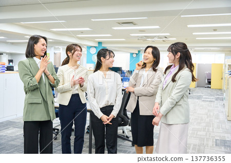 A group of female employees chatting and communicating in a brightly lit office. 137736355