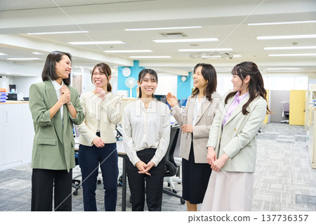 A group of female employees chatting and communicating in a brightly lit office. A group of female employees chatting and communicating in a brightly lit office. 137736357