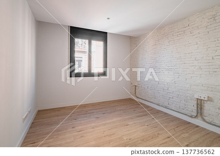 Empty room with wooden floor and white brick wall. A window allows natural light to enter. The space is minimalistic and modern, suitable for various uses. Empty room with wooden floor and white brick wall. A window allows natural light to enter. The space is minimalistic and modern, suitable for various uses. 137736562