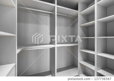 Empty modern closet with white shelves and hanging space. Minimalist design, organized storage area, suitable for home interiors. 137736567