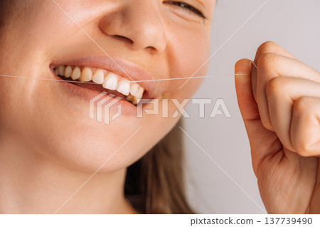 Smiling woman pulling dental floss, close up dental hygiene and prevention concept Smiling woman pulling dental floss, close up dental hygiene and prevention concept 137739490