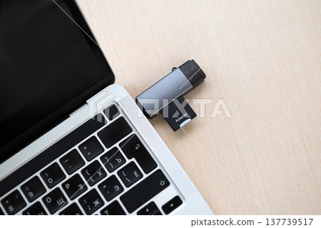 USB-C hub with SD card adapter plugged into a silver laptop on a wooden desk. Modern workspace technology. USB-C hub with SD card adapter plugged into a silver laptop on a wooden desk. Modern workspace technology. 137739517