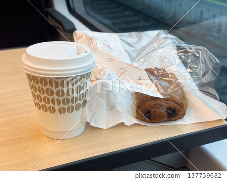 Sweet pastries in a paper bag and a glass of coffee to go on a table in a train Sweet pastries in a paper bag and a glass of coffee to go on a table in a train 137739682