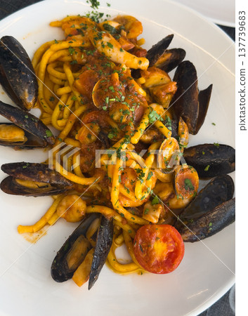 A round plate of Italian seafood pasta garnished with half a tomato on a trattoria table in Italy A round plate of Italian seafood pasta garnished with half a tomato on a trattoria table in Italy 137739683