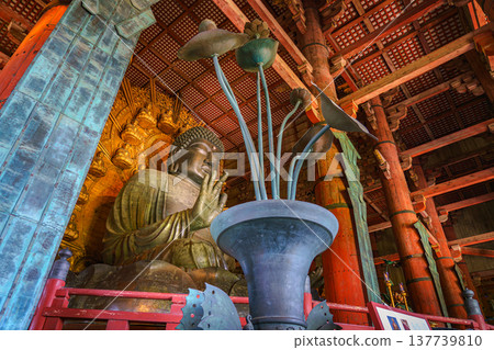 Nara, Japan - Sep 26 2024, panoramic view of giant bronze statue of Sitting Buddha Vairochana from behind decorative flower in vase, in hall of Todaiji Temple, at daytime, without people, Nara, Japan Nara, Japan - Sep 26 2024, panoramic view of giant bronze statue of Sitting Buddha Vairochana from behind decorative flower in vase, in hall of Todaiji Temple, at daytime, without people, Nara, Japan 137739810