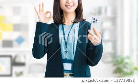 A smiling woman/businesswoman holding a smartphone and making an OK pose 137739858