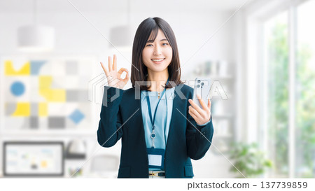 一位微笑的女人/女商人拿著智慧型手機,做出「OK」的姿勢 一位微笑的女人/女商人拿著智慧型手機,做出「OK」的姿勢 137739859