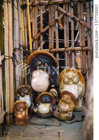 Nara, Japan - Sep 26 2024, vertical, A close-up view of a group of tanuki statues, creatures from Japanese folklore, against the background of a bamboo fence, without people, Nara, Japan Nara, Japan - Sep 26 2024, vertical, A close-up view of a group of tanuki statues, creatures from Japanese folklore, against the background of a bamboo fence, without people, Nara, Japan 137739883
