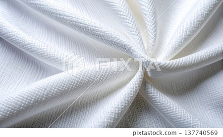 Gently folded white fabric shows off its subtle herbone weave pattern creating soft shadows and highlights on its delicate surface texture. 137740569