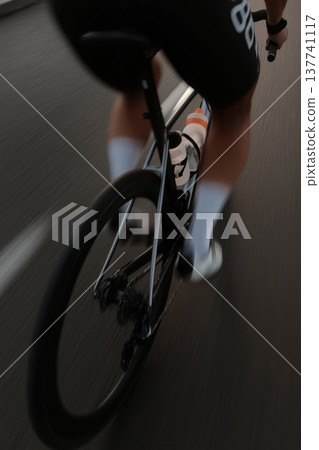 Cyclist propelling modern road bike forward on asphalt road. Cyclist riding bicycle with motion blur, emphasizing speed, fitness, and movement Cyclist propelling modern road bike forward on asphalt road. Cyclist riding bicycle with motion blur, emphasizing speed, fitness, and movement 137741117