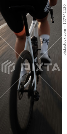 Cyclist propelling modern road bike forward on asphalt road. Cyclist riding bicycle with motion blur, emphasizing speed, fitness, and movement 137741120