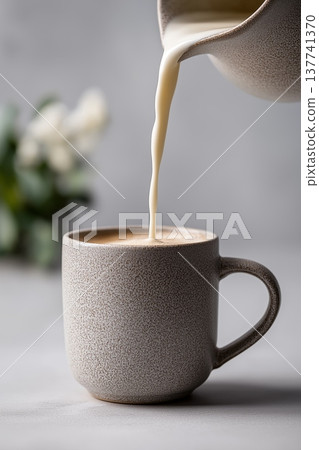 Milk pouring from pitcher into ceramic mug. Creamy dairy milk pouring from a pitcher into a ceramic mug on a gray table Milk pouring from pitcher into ceramic mug. Creamy dairy milk pouring from a pitcher into a ceramic mug on a gray table 137741370