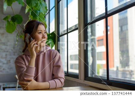 一位女士面帶微笑，靠在窗邊打電話。 137741444