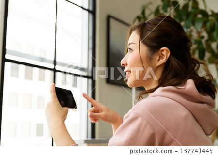 A woman is using her smartphone by the window. A woman is using her smartphone by the window. 137741445