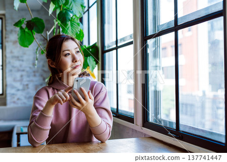 A woman who manipulates a smartphone at the window side A woman who manipulates a smartphone at the window side 137741447