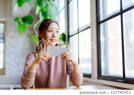 一位女士拿著智慧型手機靠在窗邊。 137741451