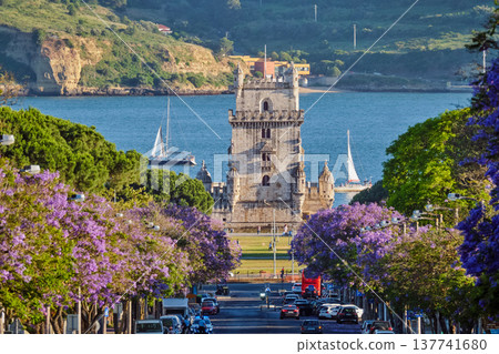 Scenic view of Belem Tower surrounded by blooming jacaranda trees, with sailboats on the Tagus River during sunset in Lisbon, Portugal. Scenic view of Belem Tower surrounded by blooming jacaranda trees, with sailboats on the Tagus River during sunset in Lisbon, Portugal. 137741680