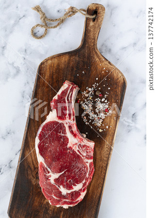 raw rib eye steak, cowboy steak, wooden chopping board, marble table, top view, no people, 137742174