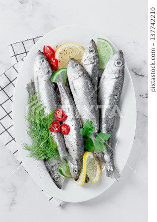 Fresh Herring fish, ready to cook, with herbs and spices, on a white platter, in the kitchen Fresh Herring fish, ready to cook, with herbs and spices, on a white platter, in the kitchen 137742210