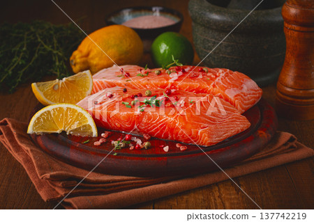 Fresh salmon fillets on a wooden platter with citrus slices and herbs arranged for cooking 137742219