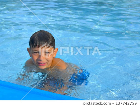 A cute little boy at the swimming pool. A smiling little kid in the water at the swimming pools. The concept of summer, summer vacations, rest, and relaxation. A cute little boy at the swimming pool. A smiling little kid in the water at the swimming pools. The concept of summer, summer vacations, rest, and relaxation. 137742759