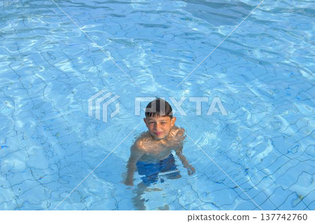 A boy in the water at a public swimming pool. A little boy plays in the pool. Copy space. The concept of summer, summer holidays, and recreation. A boy in the water at a public swimming pool. A little boy plays in the pool. Copy space. The concept of summer, summer holidays, and recreation. 137742760