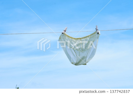 A pair of lace underwear hangs on a clothesline against a clear blue sky. This simple yet striking image evokes themes of cleanliness, freshness, and everyday life. 137742837