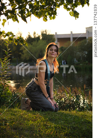 Bathed in the warm evening light, a woman kneels thoughtfully near a calm lake, her expression a mix of confidence and sincerity. The scene reflects a deep connection with one's true self, embracing Bathed in the warm evening light, a woman kneels thoughtfully near a calm lake, her expression a mix of confidence and sincerity. The scene reflects a deep connection with one's true self, embracing 137742839