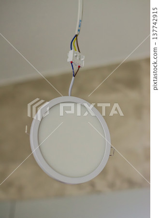 Uninstalled round white LED panel light hanging by wires from ceiling during home renovation. Uninstalled round white LED panel light hanging by wires from ceiling during home renovation. 137742915