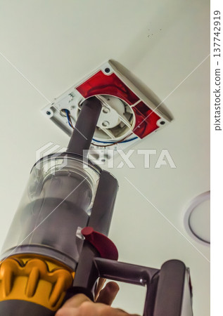 Cleaning dust from a ceiling exhaust fan ventilation system using a cordless handheld vacuum cleaner. 137742919