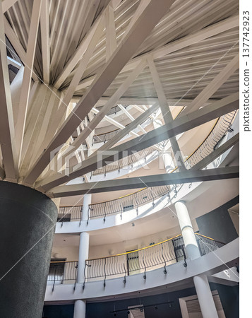 Architectural detail of a modern multi-story atrium with a complex geometric roof structure. Architectural detail of a modern multi-story atrium with a complex geometric roof structure. 137742923