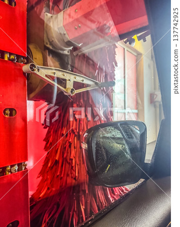 Car's perspective inside an automatic wash tunnel with large red brushes cleaning the side and window. 137742925