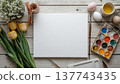 A blank white canvas on a rustic wooden table, with watercolors, flowers, and Easter decor. Concept art, education, DIY creativity, Easter decor. 137743435