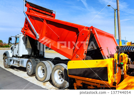 Dump truck unloading asphalt mix on construction site for road repair 137744054