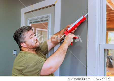 Man applies caulk to wall frame in home improvement project 137744062