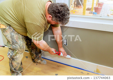 Worker applies sealant to wall at interior space during renovation process in residential home Worker applies sealant to wall at interior space during renovation process in residential home 137744063
